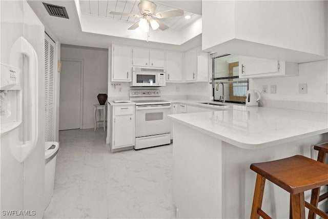kitchen with white appliances, a tray ceiling, a peninsula, white cabinets, and a sink
