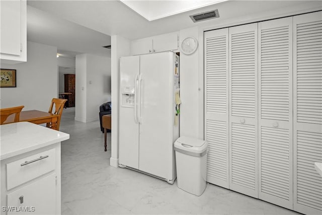 interior space with white refrigerator with ice dispenser, light countertops, white cabinetry, visible vents, and marble finish floor