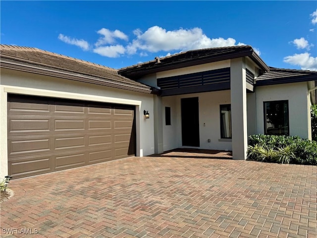 view of front facade with a tile roof, decorative driveway, a garage, and stucco siding