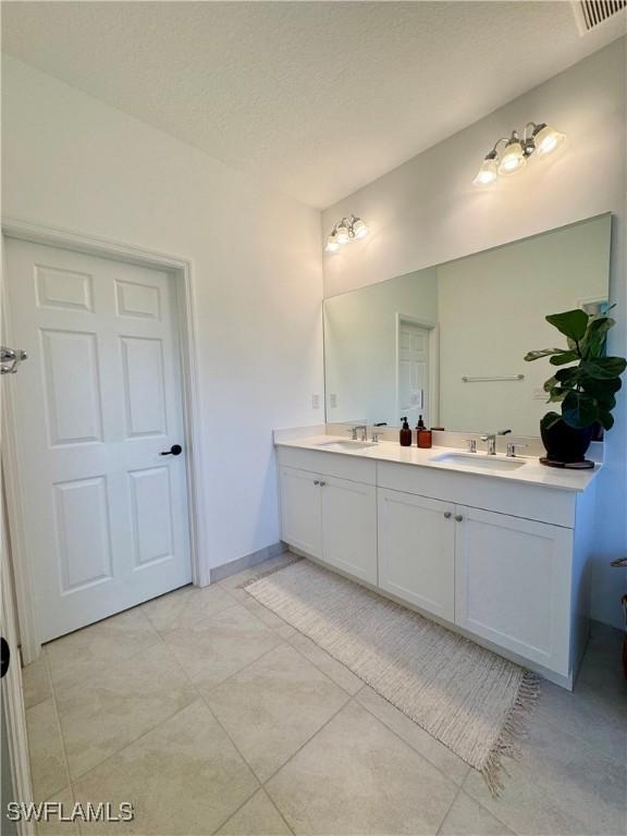 bathroom with double vanity, a sink, tile patterned flooring, and a textured ceiling