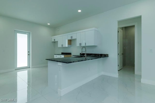 kitchen featuring dark stone countertops, baseboards, white cabinets, a sink, and marble finish floor