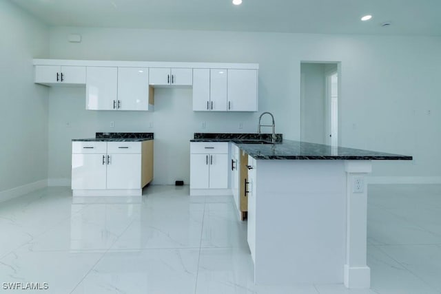 kitchen with marble finish floor, white cabinetry, a sink, and dark stone counters