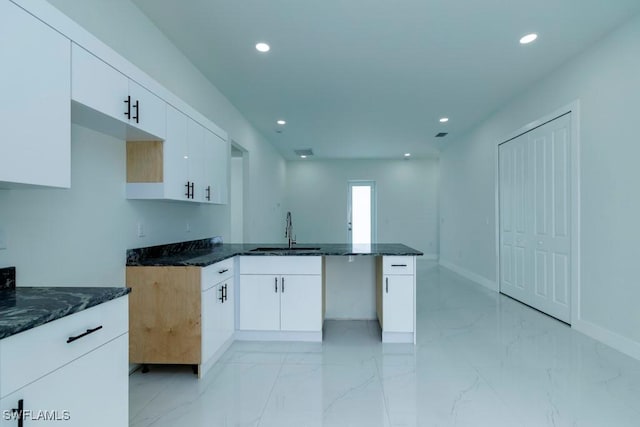 kitchen with a peninsula, marble finish floor, a sink, and dark stone counters
