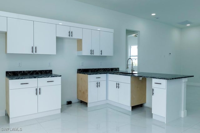 kitchen featuring a peninsula, white cabinets, dark stone countertops, marble finish floor, and a sink