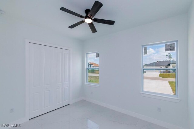 unfurnished bedroom featuring ceiling fan, a closet, marble finish floor, and baseboards
