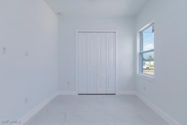 unfurnished bedroom featuring a closet, baseboards, and marble finish floor