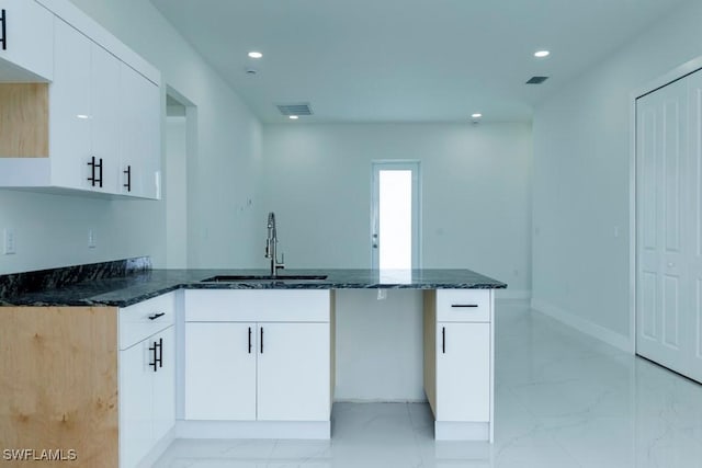 kitchen featuring a peninsula, dark stone counters, marble finish floor, and a sink