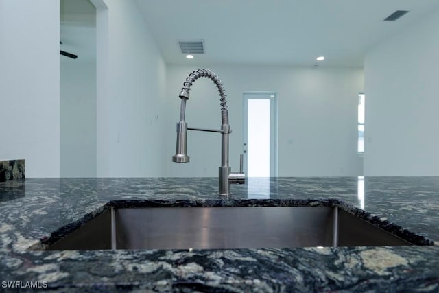 interior details with a sink, visible vents, recessed lighting, and dark stone counters