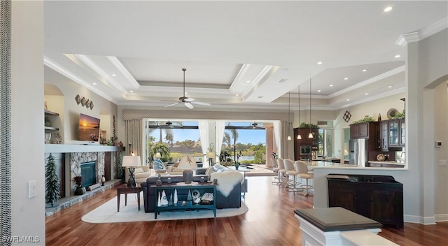 living area with ornamental molding, a tray ceiling, a ceiling fan, and wood finished floors