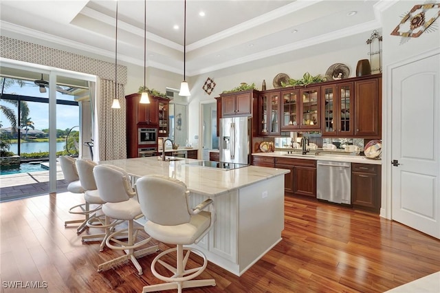 kitchen featuring a breakfast bar, crown molding, a tray ceiling, wood finished floors, and stainless steel appliances