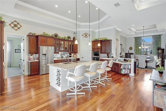 kitchen with a kitchen island with sink, visible vents, a raised ceiling, light wood finished floors, and appliances with stainless steel finishes