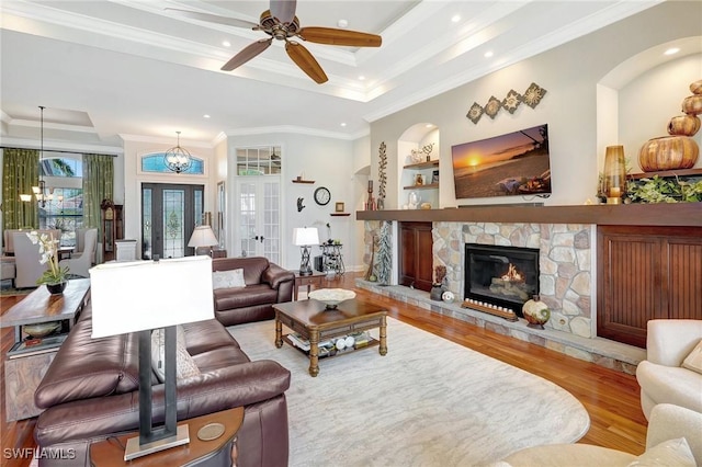 living room with a raised ceiling, ornamental molding, a stone fireplace, ceiling fan, and wood finished floors