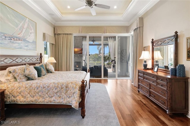 bedroom with ornamental molding, a ceiling fan, a tray ceiling, wood finished floors, and access to outside