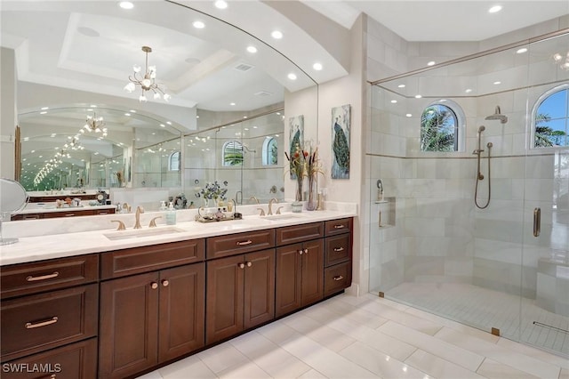 bathroom with a stall shower, double vanity, an inviting chandelier, and a sink