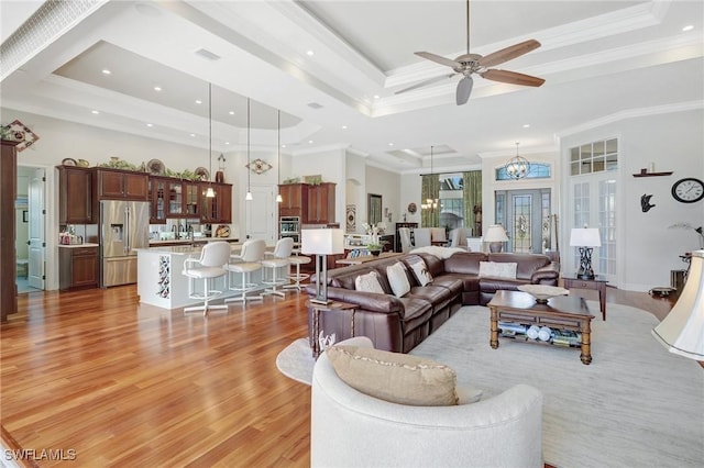 living area featuring a raised ceiling, light wood-type flooring, a high ceiling, and ceiling fan