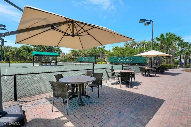 view of patio with a tennis court and fence