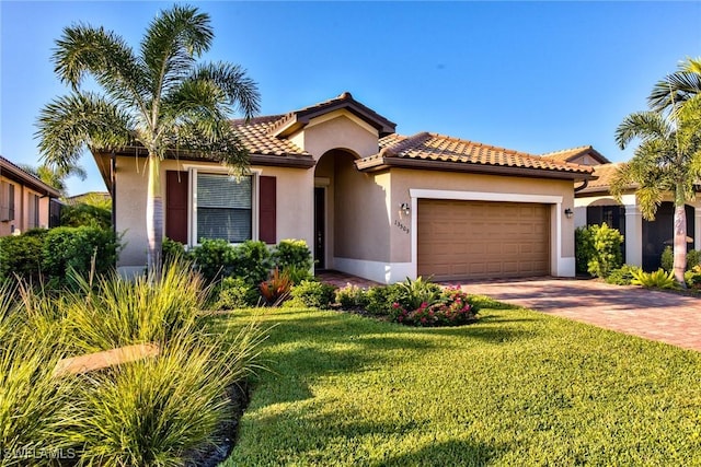 mediterranean / spanish-style house with a front yard, stucco siding, an attached garage, a tiled roof, and decorative driveway