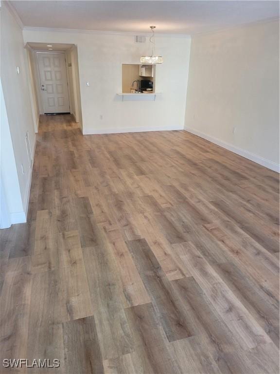 unfurnished living room featuring baseboards, a sink, a chandelier, crown molding, and wood finished floors