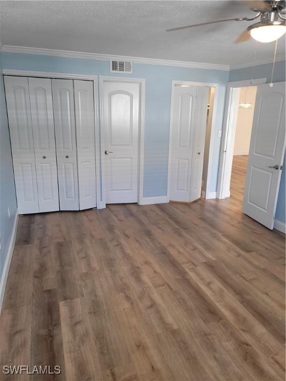 unfurnished bedroom with a ceiling fan, baseboards, ornamental molding, visible vents, and wood finished floors