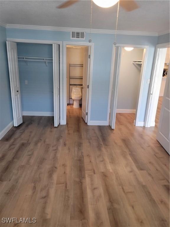 unfurnished bedroom with wood finished floors, ornamental molding, ensuite bath, visible vents, and baseboards