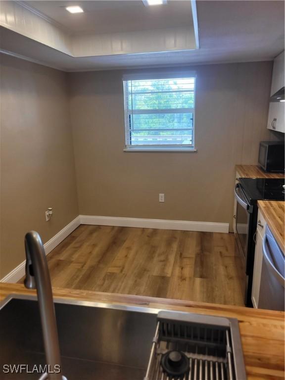 kitchen featuring wood finished floors, stainless steel dishwasher, black electric range, and baseboards