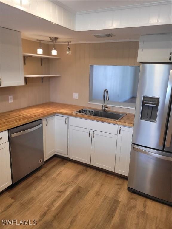 kitchen with a sink, light wood-type flooring, white cabinetry, wooden counters, and appliances with stainless steel finishes