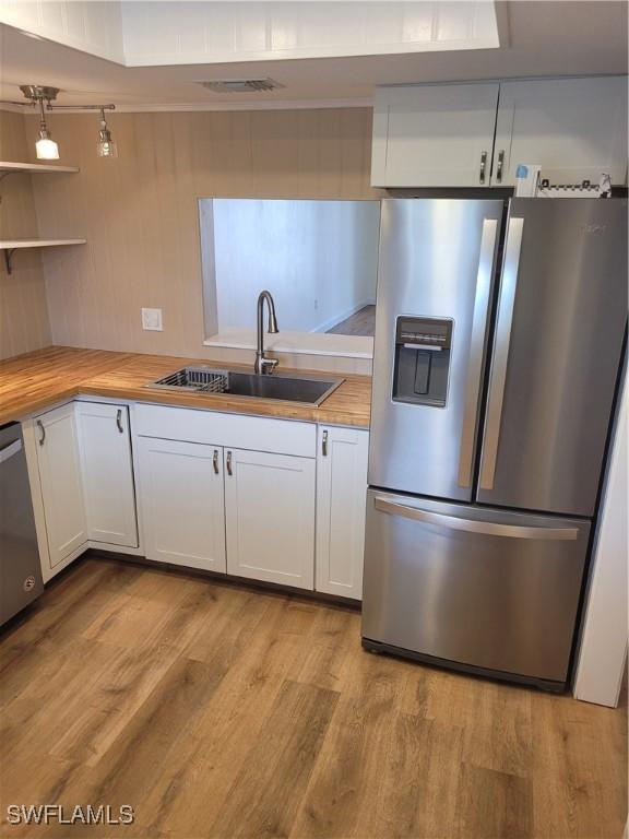 kitchen featuring a sink, appliances with stainless steel finishes, white cabinetry, wooden counters, and light wood-style floors