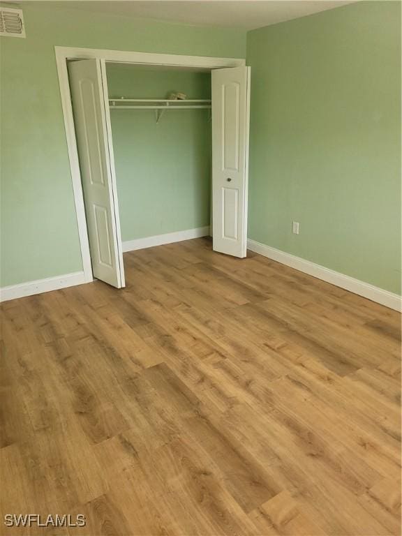 unfurnished bedroom with baseboards, a closet, visible vents, and wood finished floors