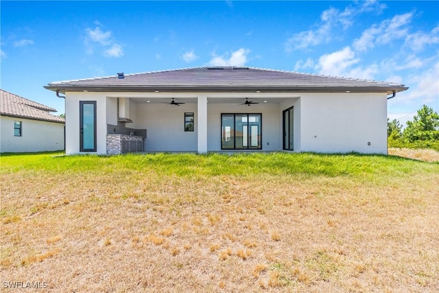 back of house featuring a lawn, a ceiling fan, and stucco siding