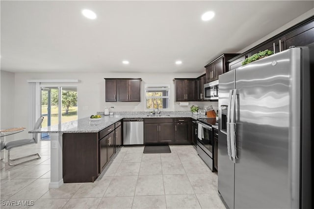 kitchen with light tile patterned floors, stainless steel appliances, a sink, a peninsula, and dark brown cabinetry