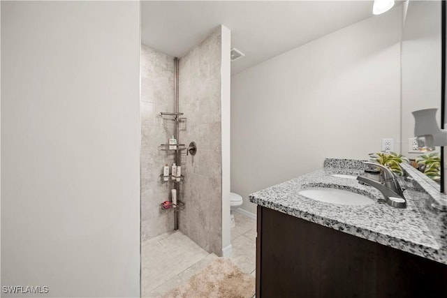 full bathroom featuring toilet, tiled shower, vanity, tile patterned flooring, and baseboards