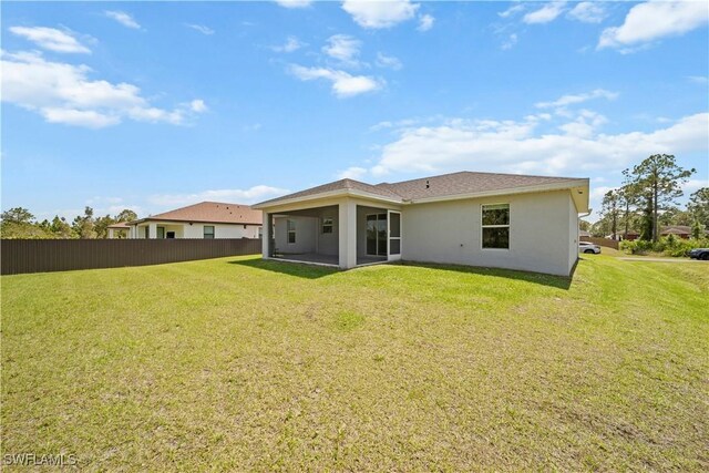 back of house featuring stucco siding, fence, and a lawn