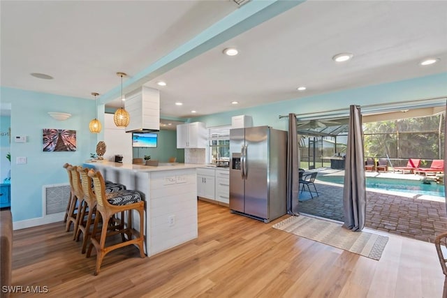 kitchen with a peninsula, white cabinetry, visible vents, stainless steel fridge, and light wood finished floors
