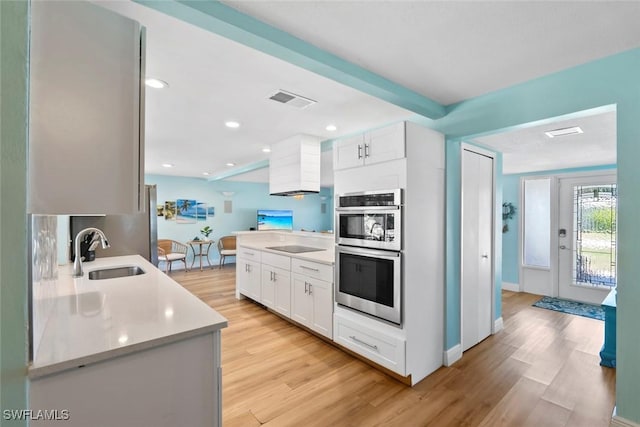 kitchen featuring light wood-style flooring, light countertops, visible vents, double oven, and a sink