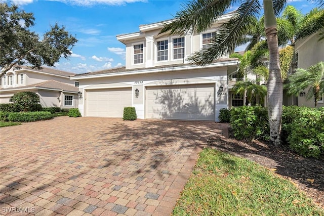 traditional home with a garage, stucco siding, and decorative driveway