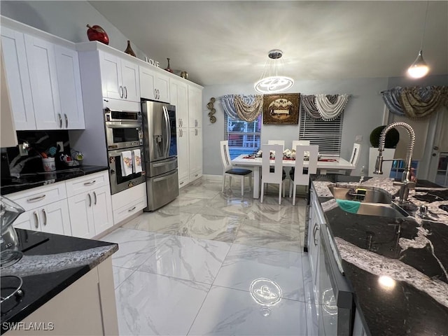 kitchen with a sink, marble finish floor, white cabinets, hanging light fixtures, and appliances with stainless steel finishes