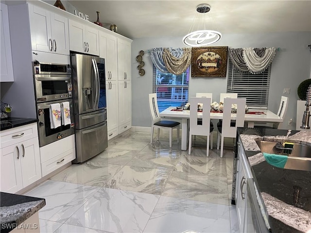 kitchen with a notable chandelier, hanging light fixtures, dark stone counters, stainless steel appliances, and white cabinets
