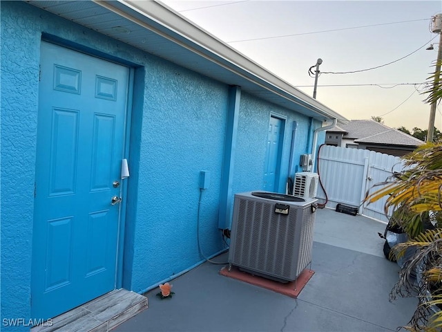 exterior entry at dusk with ac unit, cooling unit, stucco siding, and fence