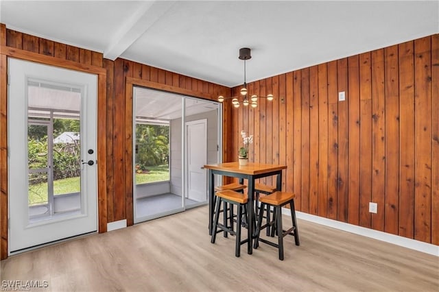 dining room with beamed ceiling, light wood finished floors, wooden walls, and baseboards