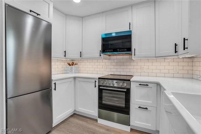 kitchen featuring light wood-type flooring, white cabinets, appliances with stainless steel finishes, and light countertops