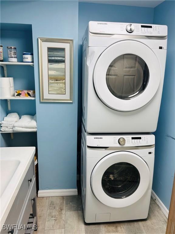 laundry room featuring baseboards, stacked washing maching and dryer, cabinet space, and light wood-style flooring