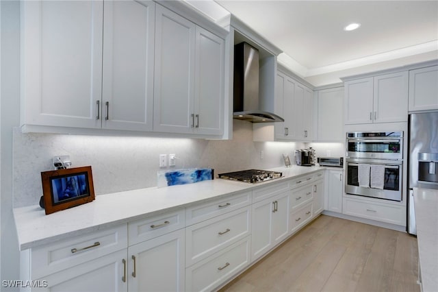 11607 Periwinkle Dr, Naples, FL 34120 - kitchen with light wood-style flooring, white cabinets, wall chimney range hood, appliances with stainless steel finishes, and recessed lighting