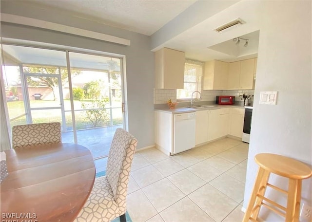kitchen featuring white dishwasher, tasteful backsplash, a sink, light countertops, and light tile patterned floors