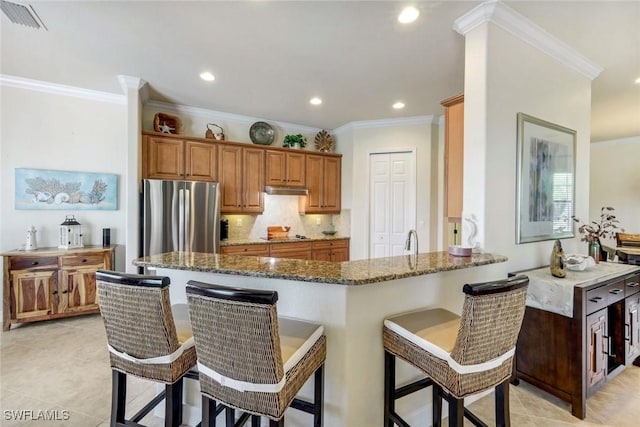 kitchen featuring a kitchen breakfast bar, ornamental molding, dark stone countertops, freestanding refrigerator, and visible vents