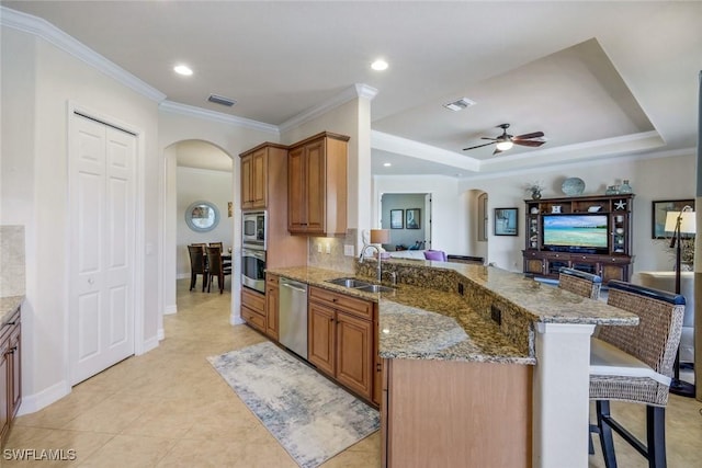 kitchen featuring arched walkways, a breakfast bar, appliances with stainless steel finishes, a sink, and open floor plan