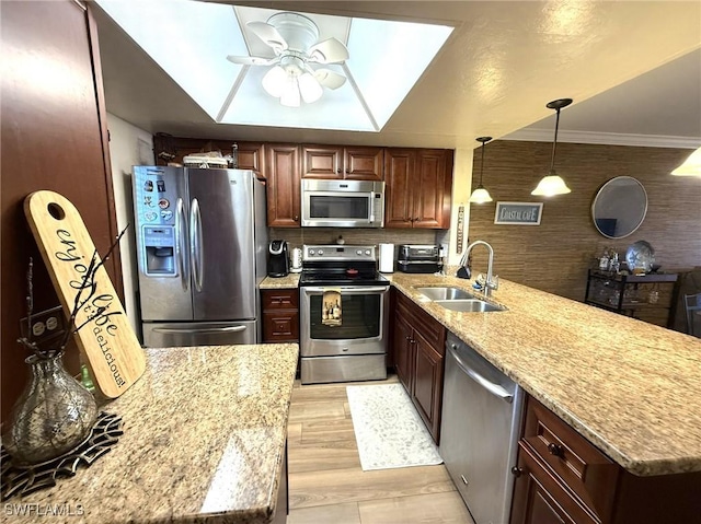 kitchen with a peninsula, a ceiling fan, stainless steel appliances, light wood finished floors, and a sink