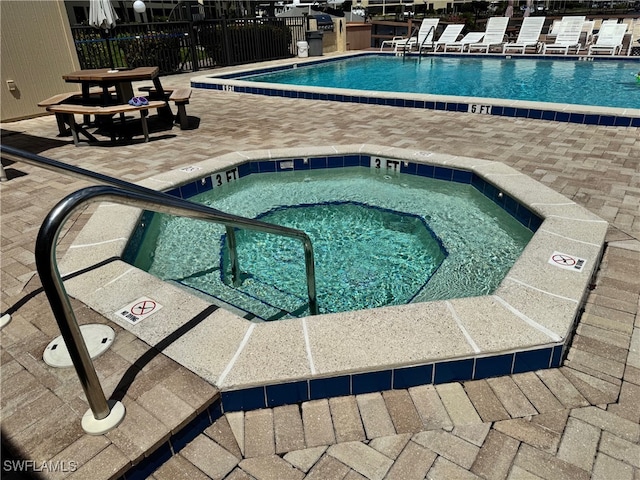 community pool with a hot tub, fence, and a patio area