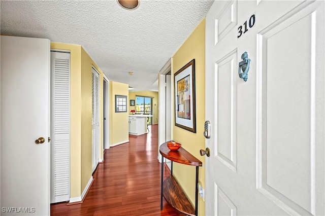 hall featuring a textured ceiling, baseboards, and dark wood-type flooring