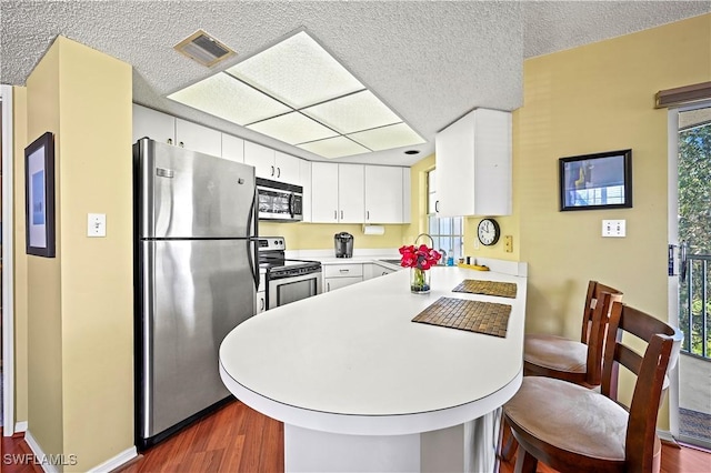 kitchen featuring white cabinets, appliances with stainless steel finishes, light countertops, dark wood finished floors, and a peninsula