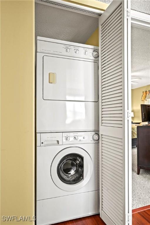 clothes washing area featuring laundry area, a textured ceiling, dark wood-type flooring, and stacked washer / dryer